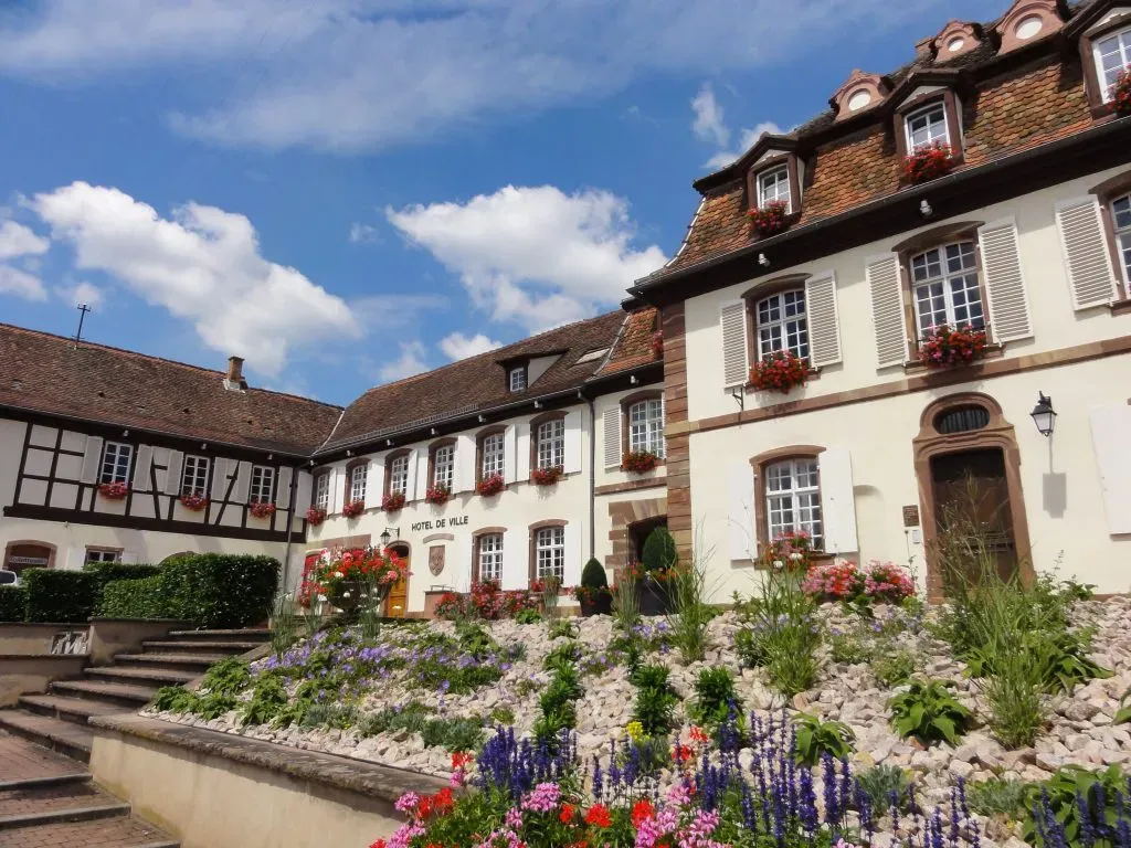 Hôtel de ville de Marlenheim entouré de parterres de fleurs et aménagements paysagers.