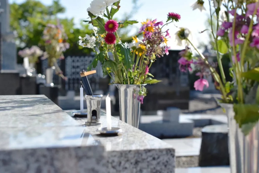 Fleurs fraîches et bougies de recueillement posées sur une pierre tombale au cimetière.