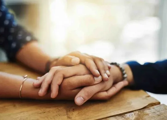 Mains jointes sur une table en bois, symbole de réconfort et de soutien dans le deuil.